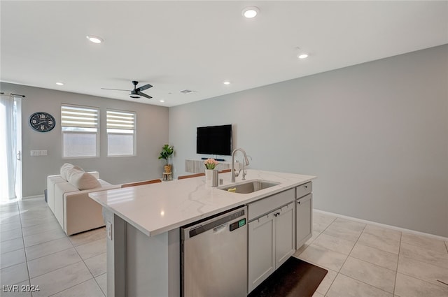 kitchen with light stone counters, an island with sink, stainless steel dishwasher, light tile patterned flooring, and sink