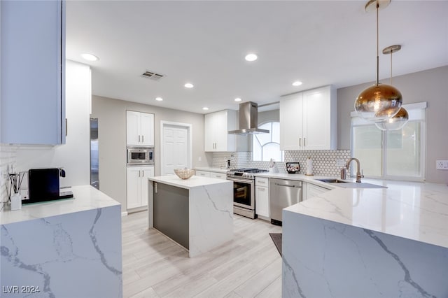 kitchen featuring light stone countertops, pendant lighting, wall chimney range hood, and appliances with stainless steel finishes