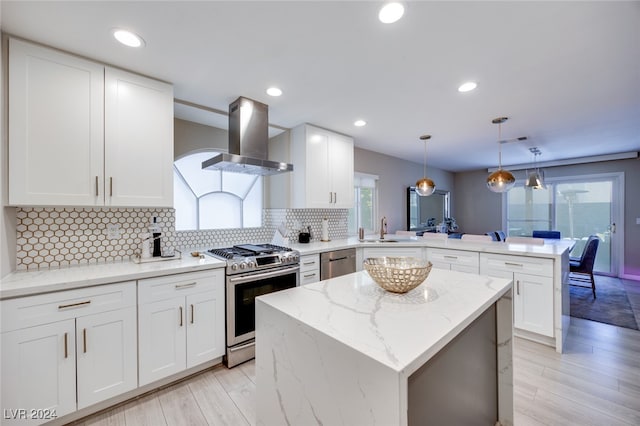 kitchen featuring light hardwood / wood-style flooring, decorative light fixtures, kitchen peninsula, island exhaust hood, and stainless steel appliances