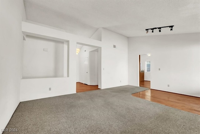 spare room with a textured ceiling, wood-type flooring, vaulted ceiling, and track lighting