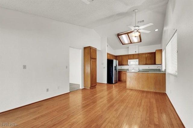 kitchen featuring white appliances, a skylight, kitchen peninsula, light hardwood / wood-style floors, and ceiling fan