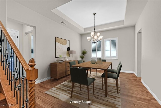 dining space featuring a chandelier, light wood-type flooring, and a raised ceiling