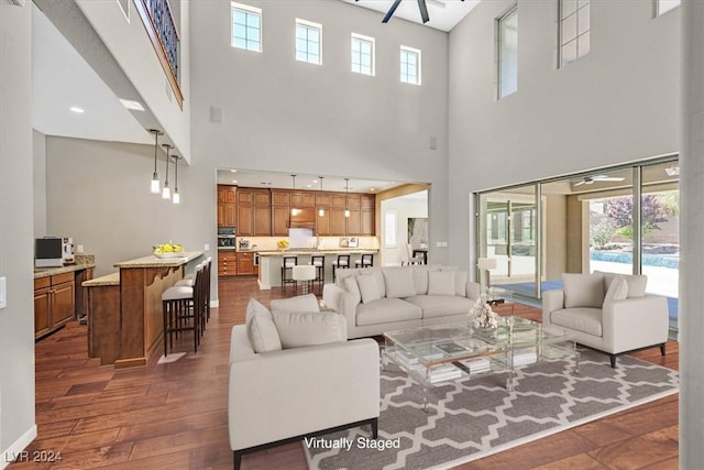 living room with ceiling fan, a high ceiling, and dark hardwood / wood-style floors