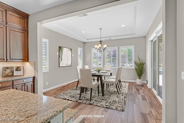 dining space featuring a raised ceiling, light hardwood / wood-style floors, and an inviting chandelier