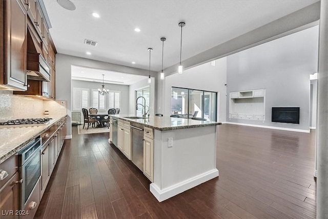 kitchen with pendant lighting, a kitchen island with sink, dark wood-type flooring, sink, and light stone counters