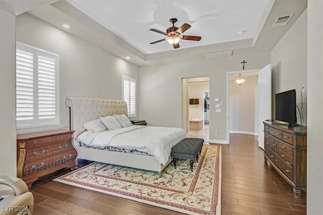 bedroom with ceiling fan, dark hardwood / wood-style floors, connected bathroom, and a tray ceiling