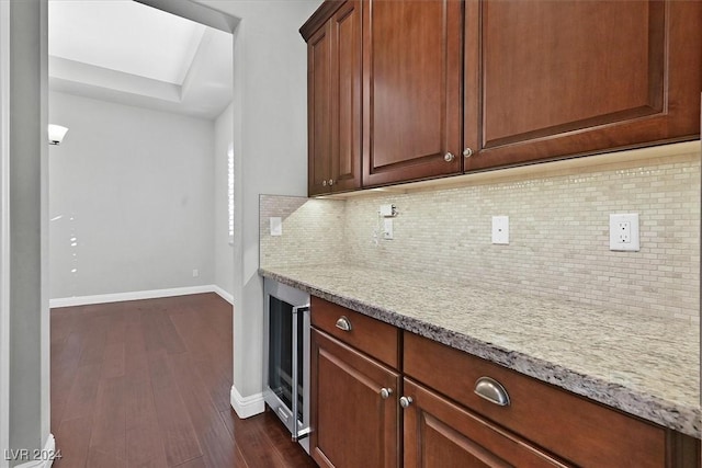 kitchen with light stone countertops, dark wood-type flooring, wine cooler, and tasteful backsplash