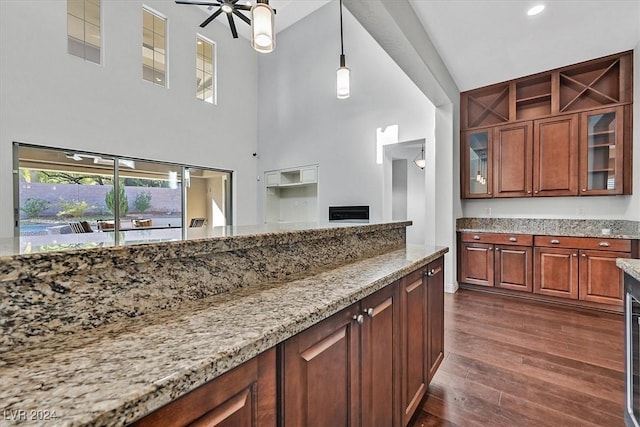 kitchen featuring light stone countertops, a towering ceiling, ceiling fan, dark wood-type flooring, and pendant lighting