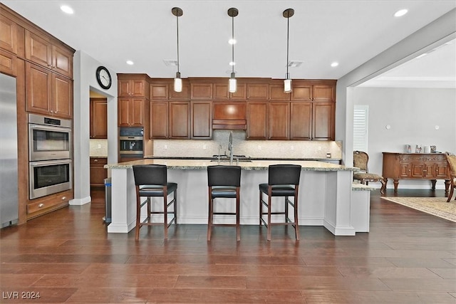 kitchen with light stone countertops, hanging light fixtures, a large island with sink, and dark wood-type flooring