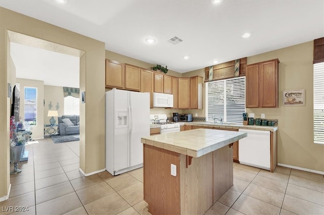 kitchen with light tile patterned floors, tile countertops, sink, a center island, and white appliances