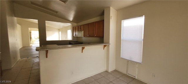 kitchen featuring light tile patterned flooring, lofted ceiling, a kitchen bar, and kitchen peninsula