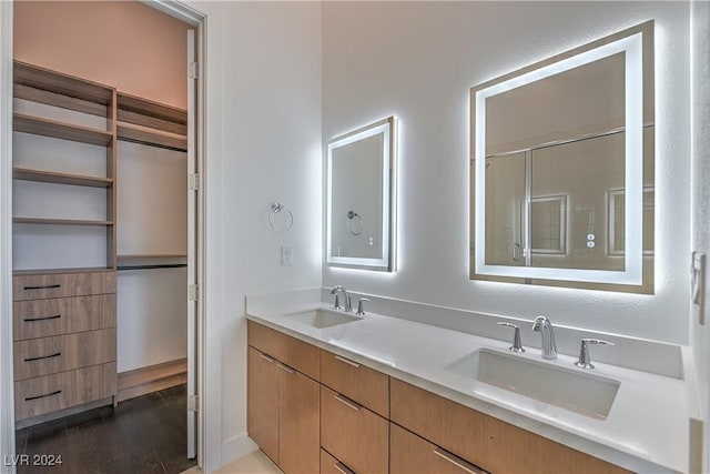 bathroom with double vanity, wood finished floors, a sink, and a shower with shower door