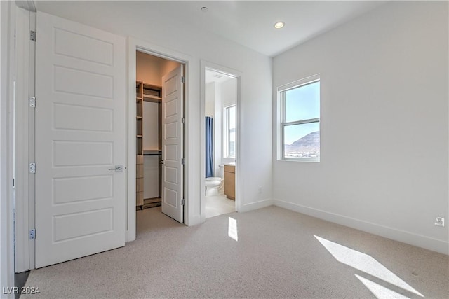 unfurnished bedroom with a walk in closet, recessed lighting, a closet, light colored carpet, and baseboards