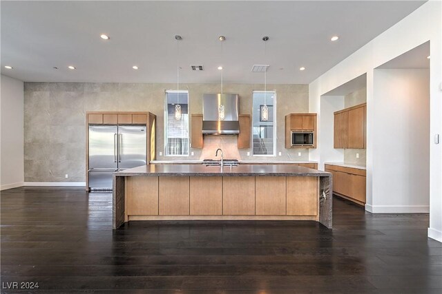 kitchen featuring a large island, dark wood-type flooring, hanging light fixtures, built in appliances, and wall chimney exhaust hood