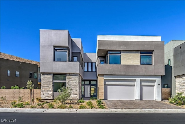 contemporary home with stone siding, driveway, an attached garage, and stucco siding