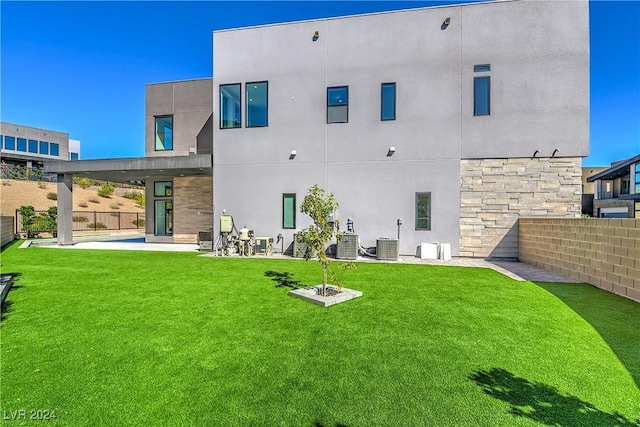 rear view of property with fence, a yard, stone siding, stucco siding, and a patio area