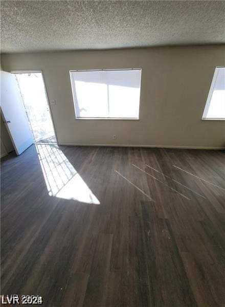 empty room with dark hardwood / wood-style flooring, plenty of natural light, and a textured ceiling