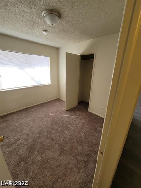 unfurnished bedroom with a closet, a textured ceiling, and dark colored carpet