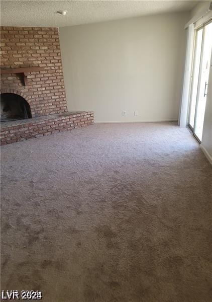 unfurnished living room featuring carpet flooring, a brick fireplace, and a textured ceiling