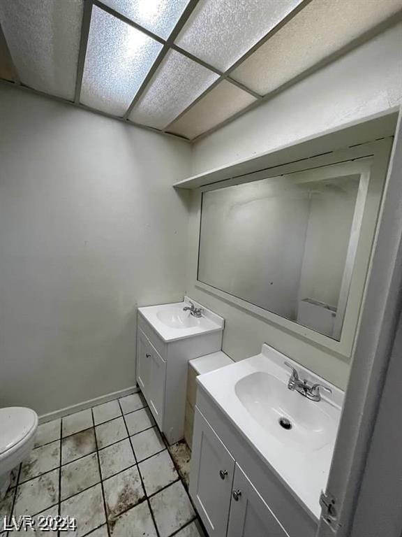 bathroom with vanity, toilet, tile patterned flooring, and a drop ceiling