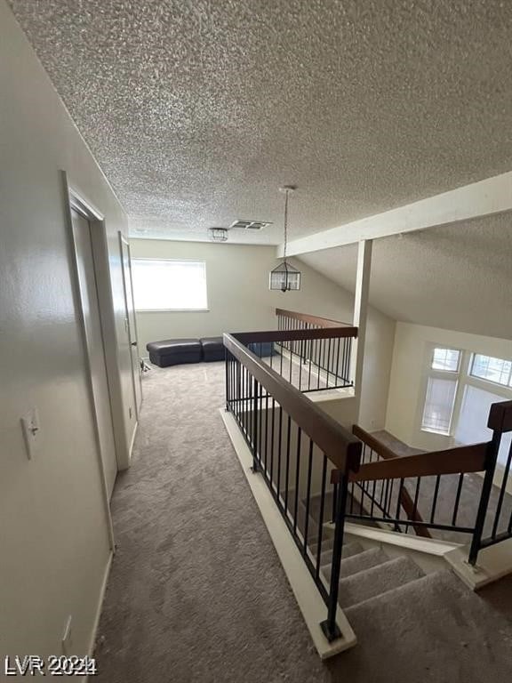 corridor featuring lofted ceiling, a textured ceiling, and carpet floors