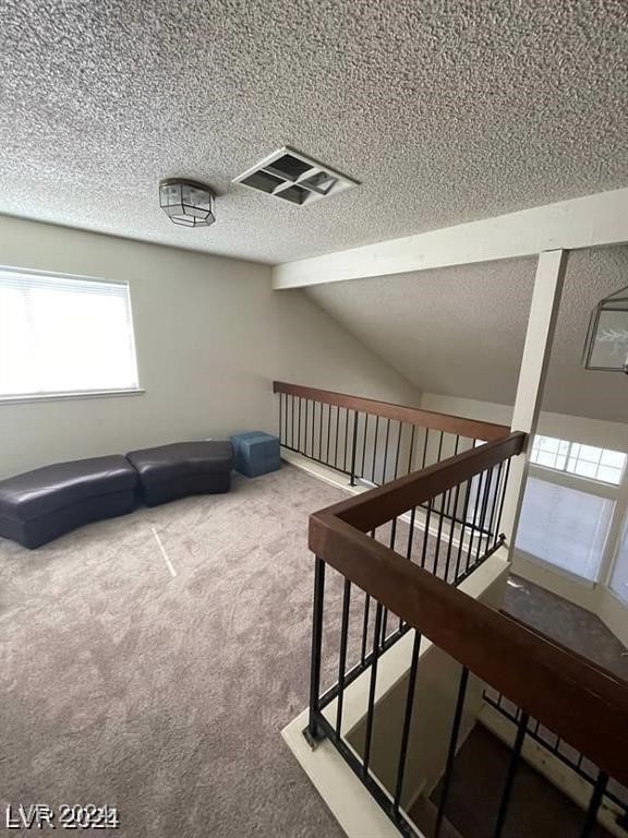 interior space featuring a textured ceiling, lofted ceiling with beams, and carpet flooring