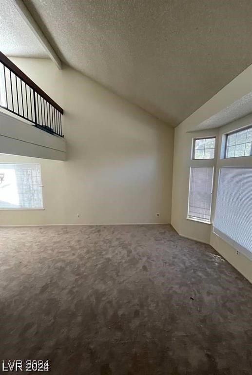 unfurnished living room featuring lofted ceiling with beams, carpet, and a textured ceiling