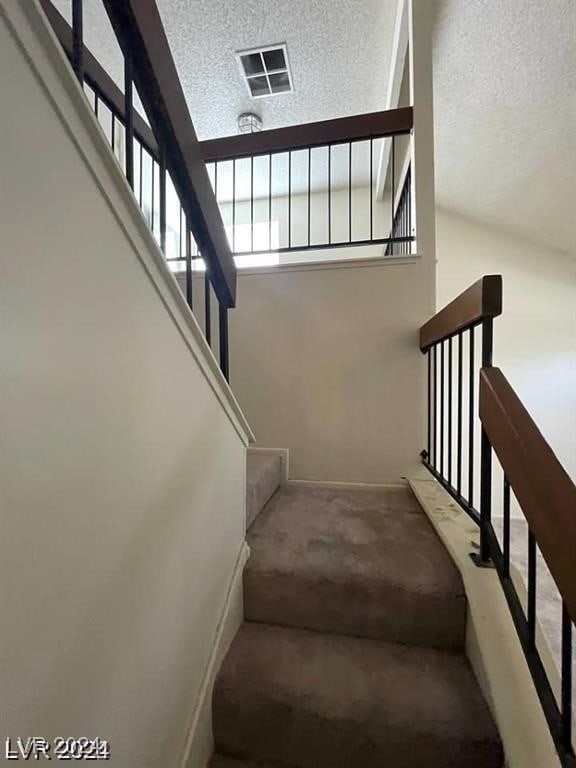 staircase featuring vaulted ceiling, carpet flooring, and a textured ceiling