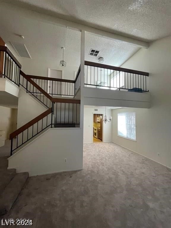 unfurnished living room featuring a textured ceiling, beam ceiling, high vaulted ceiling, and carpet flooring