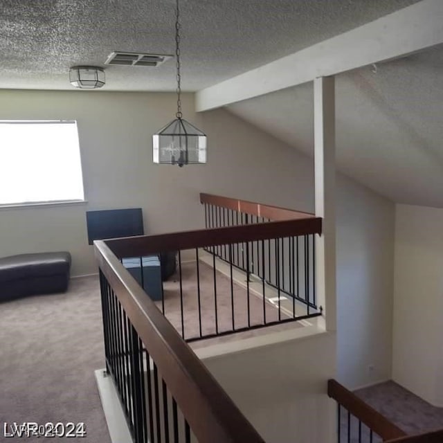 stairway with a chandelier, a textured ceiling, carpet floors, and vaulted ceiling with beams