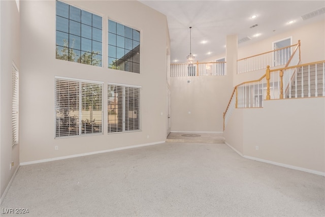 unfurnished living room featuring an inviting chandelier, carpet floors, and a high ceiling