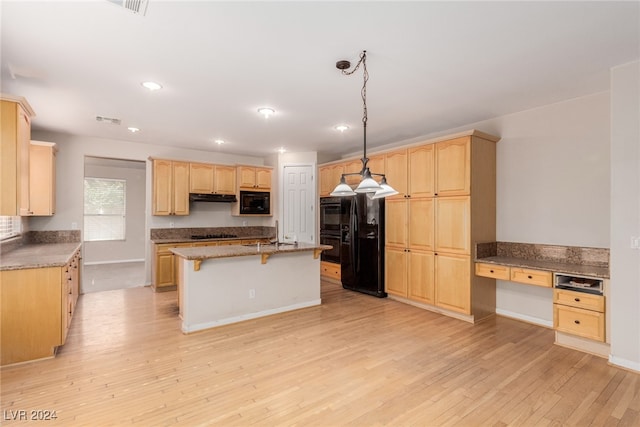 kitchen with built in desk, light hardwood / wood-style flooring, black appliances, pendant lighting, and a center island