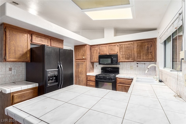 kitchen with sink, tasteful backsplash, tile countertops, vaulted ceiling, and black appliances