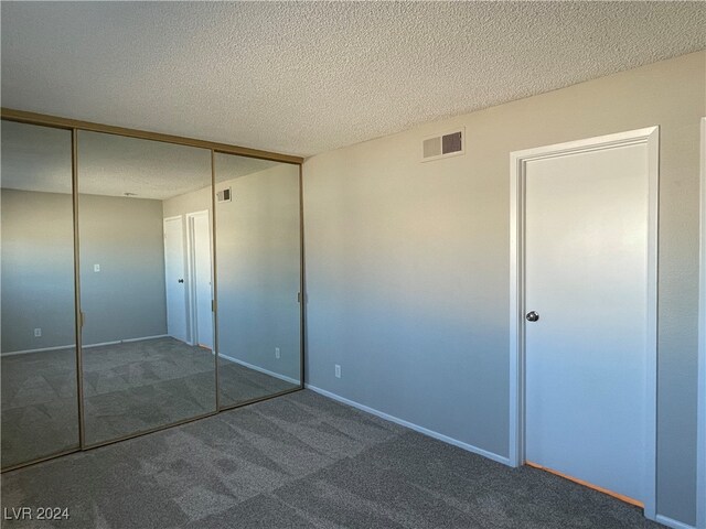 unfurnished bedroom with a closet, a textured ceiling, and dark carpet