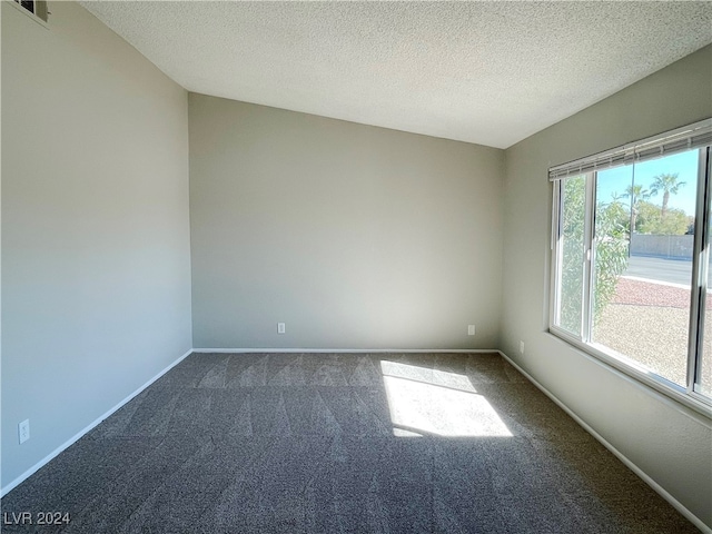 empty room featuring a textured ceiling, vaulted ceiling, and dark colored carpet