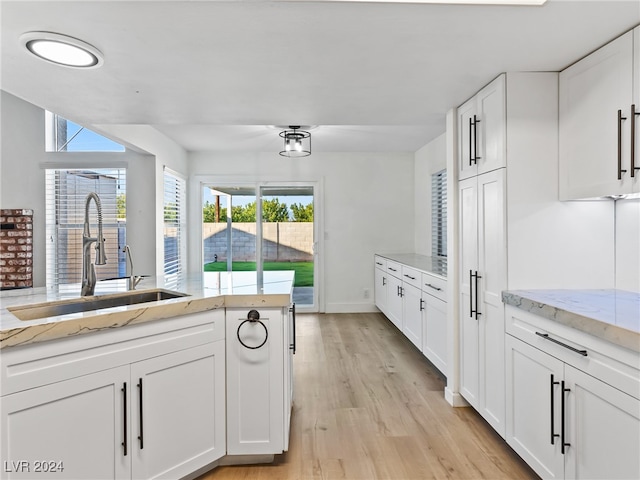 kitchen with white cabinets, light stone countertops, light wood-type flooring, and sink