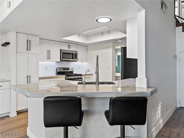 kitchen featuring kitchen peninsula, appliances with stainless steel finishes, a breakfast bar, light hardwood / wood-style floors, and white cabinetry