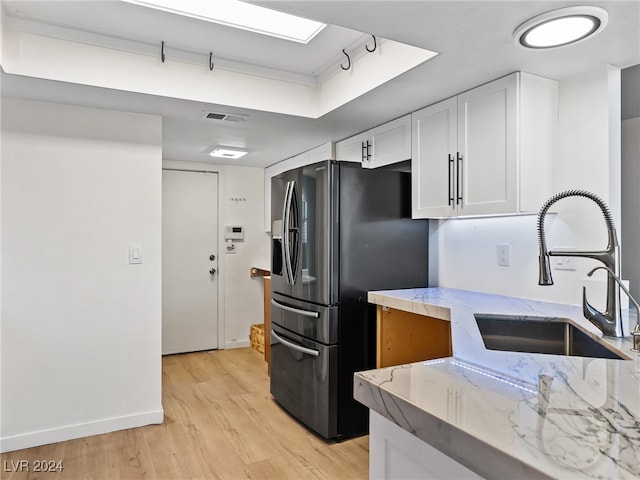 kitchen with sink, stainless steel refrigerator with ice dispenser, light hardwood / wood-style flooring, light stone countertops, and white cabinetry