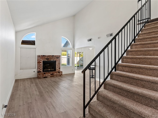 stairs featuring a fireplace, wood-type flooring, and high vaulted ceiling