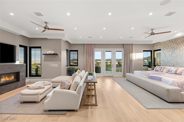 bedroom with access to outside, a tiled fireplace, french doors, and light wood-type flooring