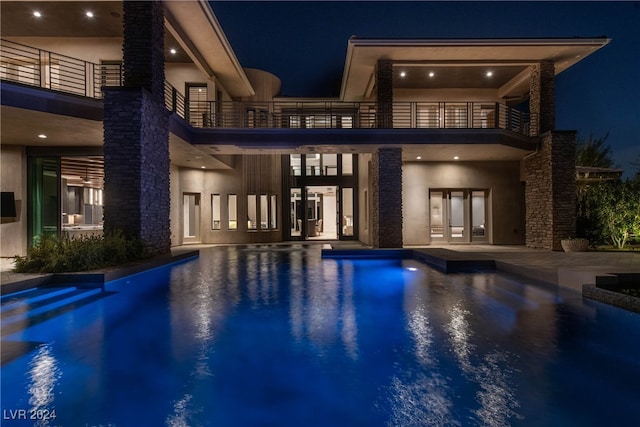 back house at night featuring a balcony and french doors