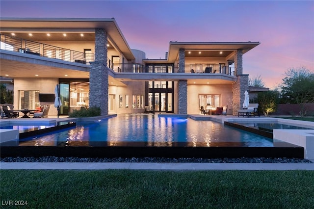 back house at dusk with a balcony and a patio area