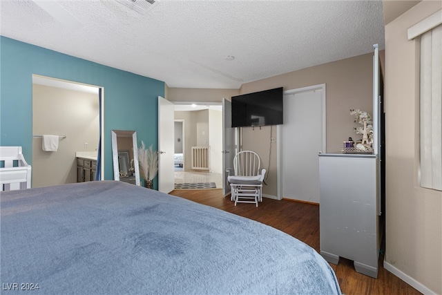 bedroom featuring dark wood-type flooring, ensuite bathroom, and a textured ceiling