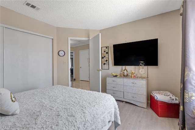 bedroom with a closet, a textured ceiling, and light wood-type flooring