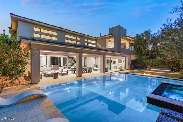 back house at dusk featuring a swimming pool with hot tub, an outdoor living space, and a patio