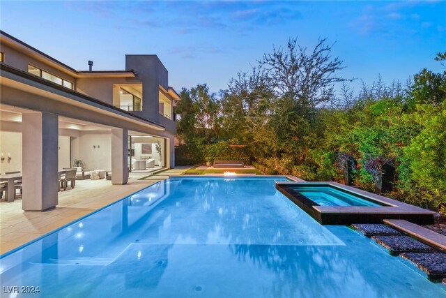 pool at dusk featuring a patio and an in ground hot tub