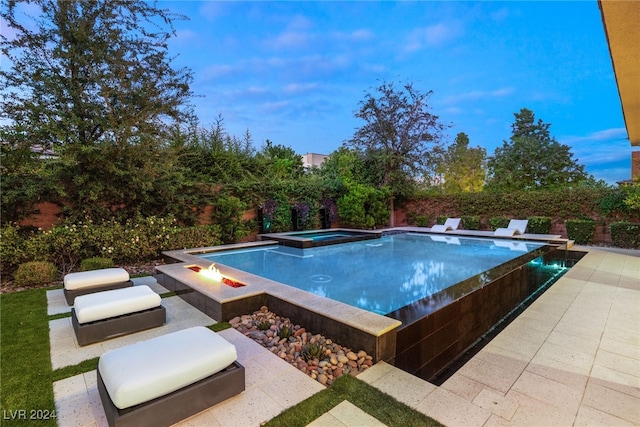 pool at dusk with an in ground hot tub and a patio