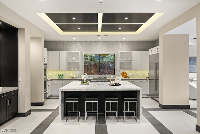 kitchen with backsplash, a kitchen breakfast bar, light stone countertops, stainless steel appliances, and a center island