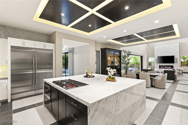 kitchen with a large island, white cabinets, a large fireplace, built in appliances, and light stone counters