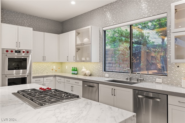 kitchen with white cabinetry, stainless steel appliances, sink, and light stone counters